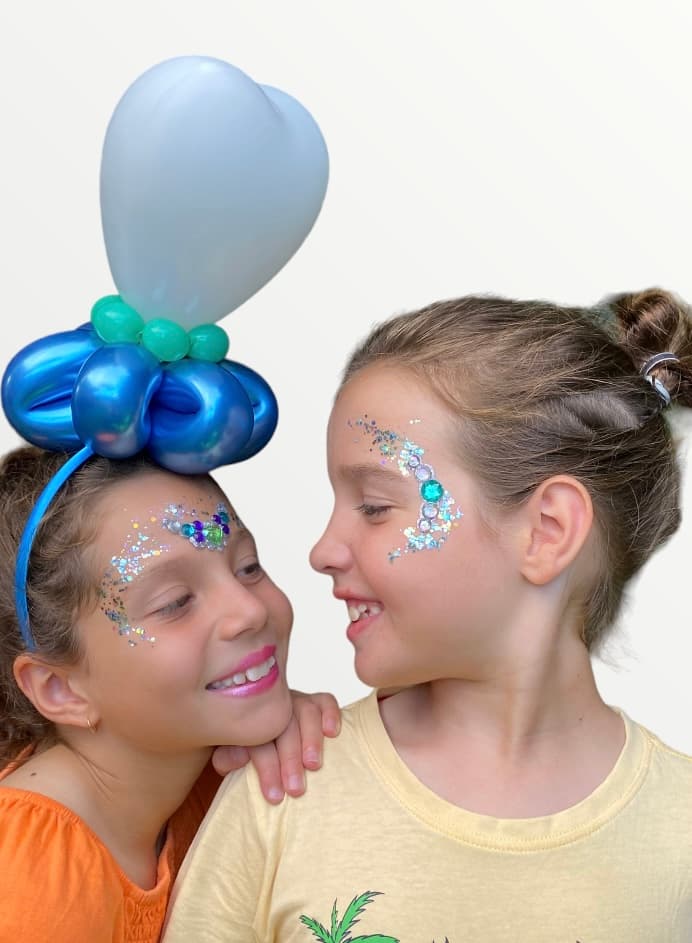 Two girls with glitter face art and balloons